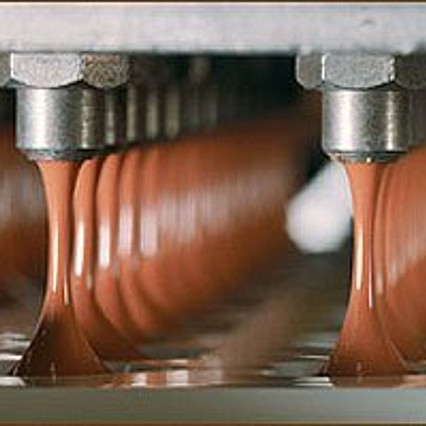 Die älteste Art des Formens: in flache Formen, die die Negativform des fertigen Produktes darstellen, wird die duftende, flüssige Schokoladenmasse eindosiert.